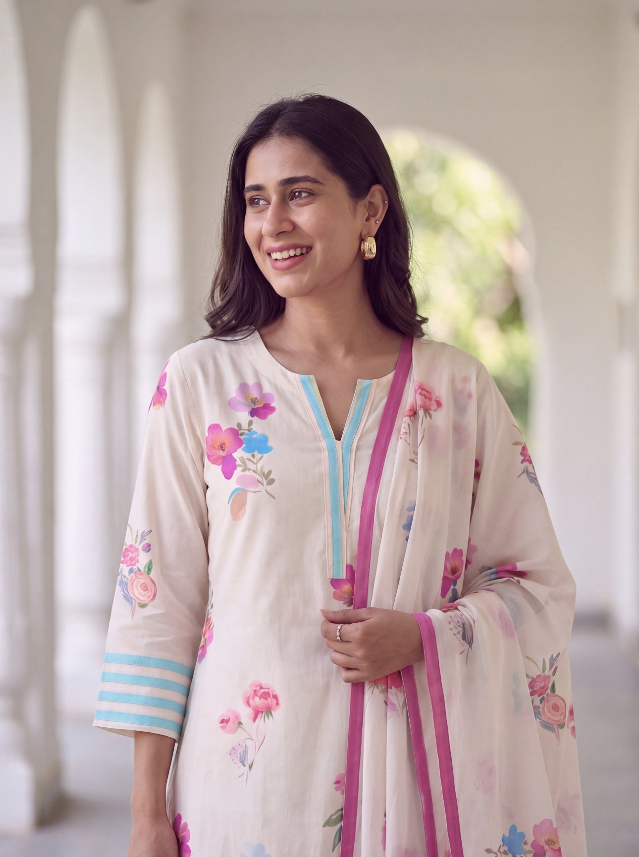 Woman smiling in ivory floral kurta with pink bordered floral dupatta
